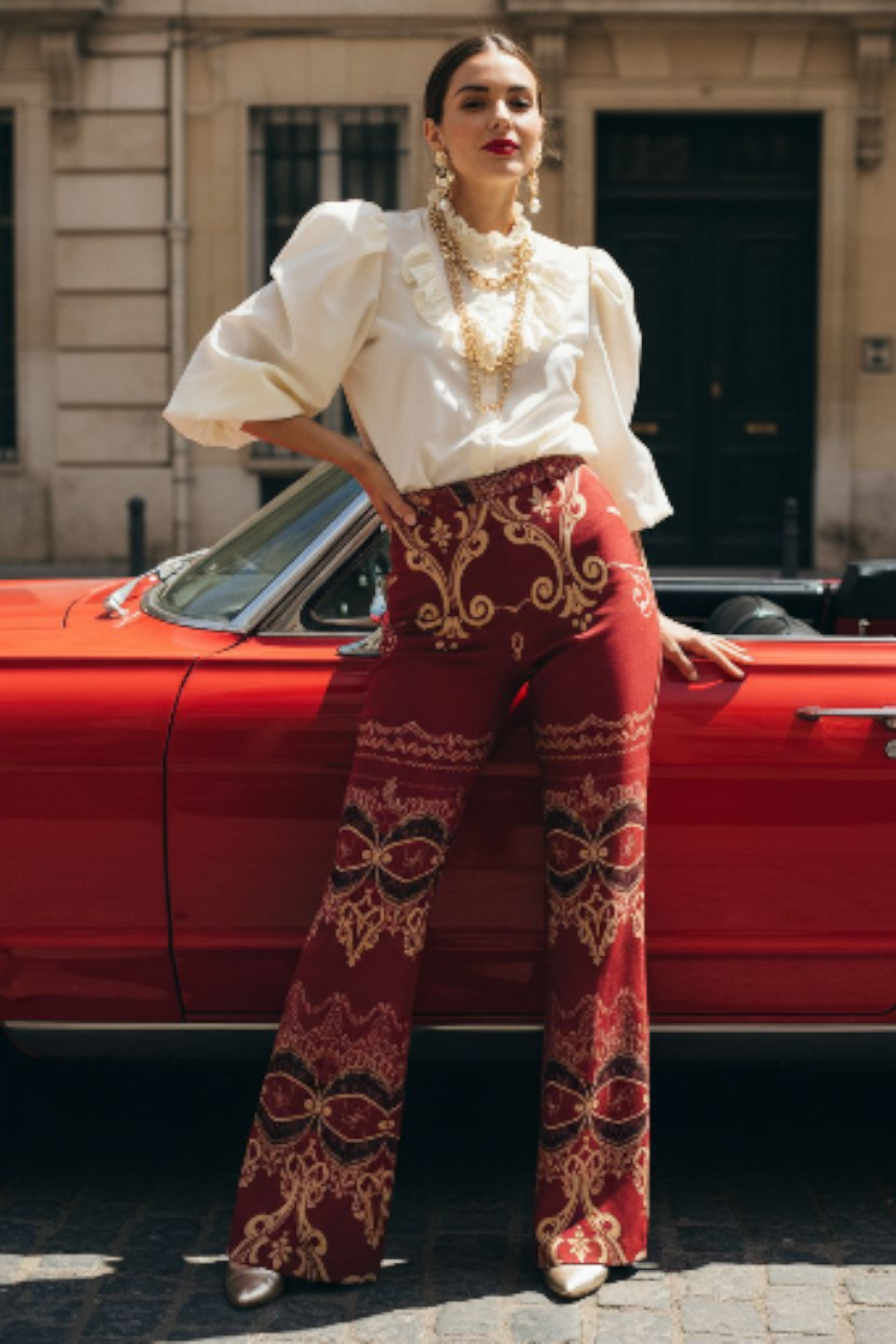 Burgundy high waist wide leg pants with intricate gold patterns worn with white puff sleeve blouse