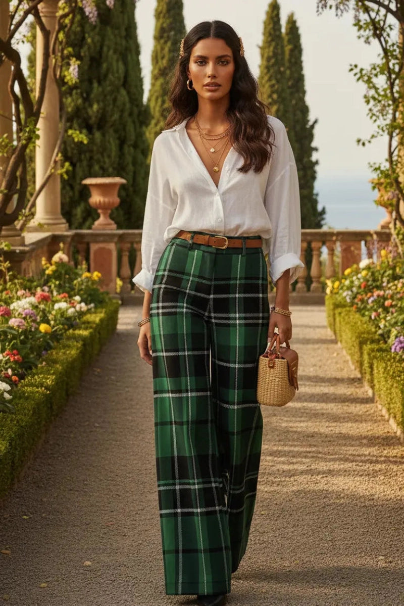Woman wearing green tartan wide leg trousers with a white blouse and brown belt in a garden setting