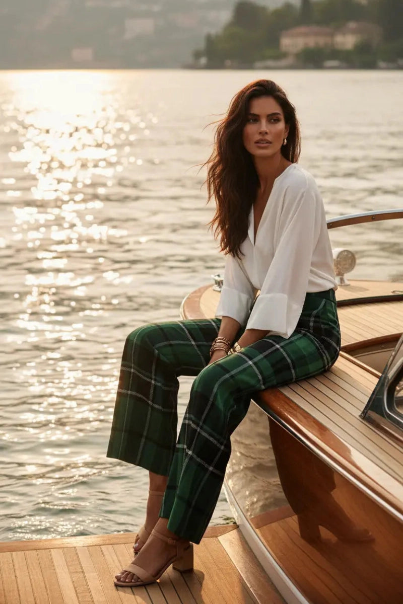 Woman wearing green tartan wide leg trousers sitting on a boat deck by the water at sunset