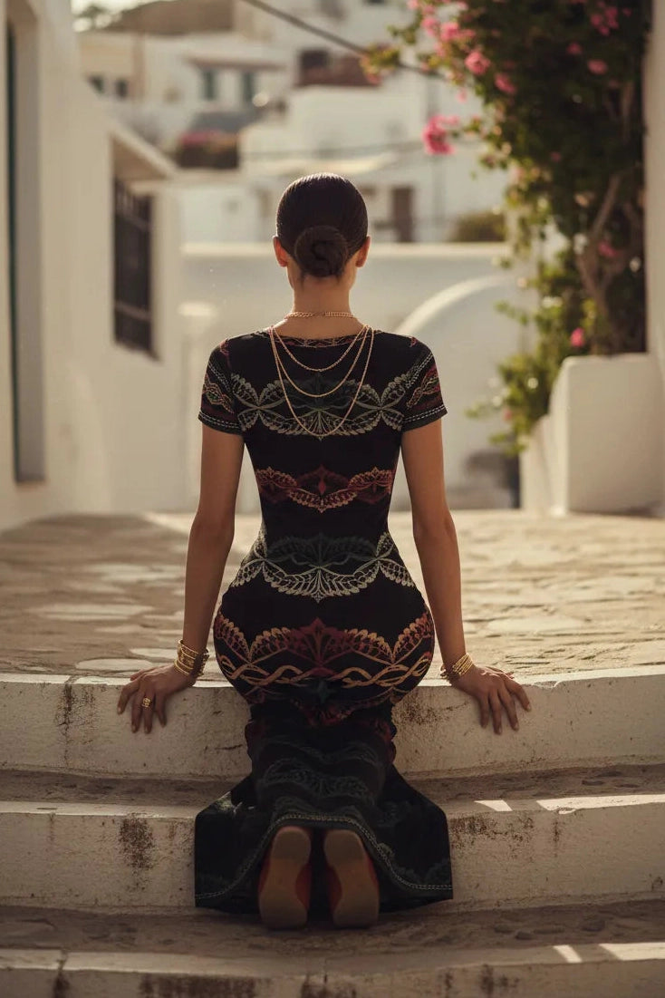Woman wearing elegant short sleeve midi dress with intricate patterns sitting on stone steps outdoors