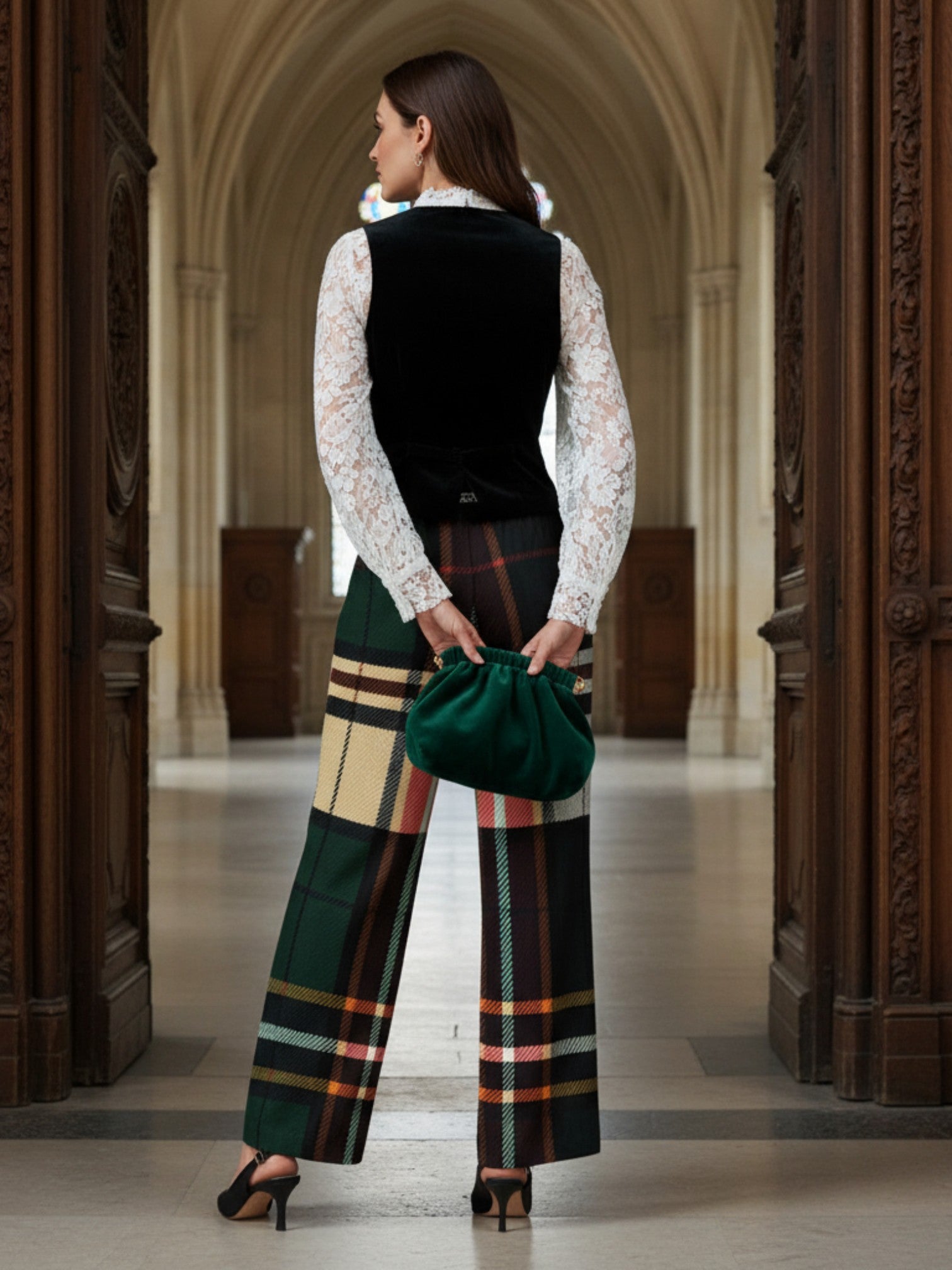 Women wearing women's Green tartan wide-leg trousers with a white lace blouse and black vest holding a green bag