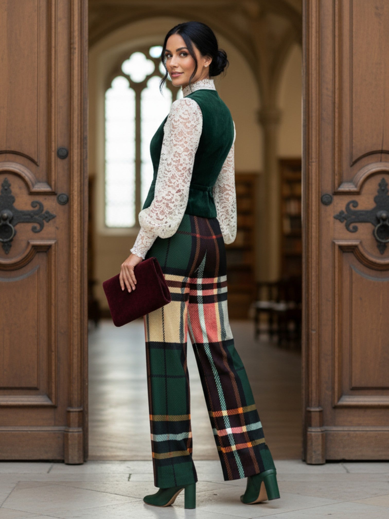 Women's green tartan wide-leg trousers styled with a lace blouse and green heels in a classic indoor setting